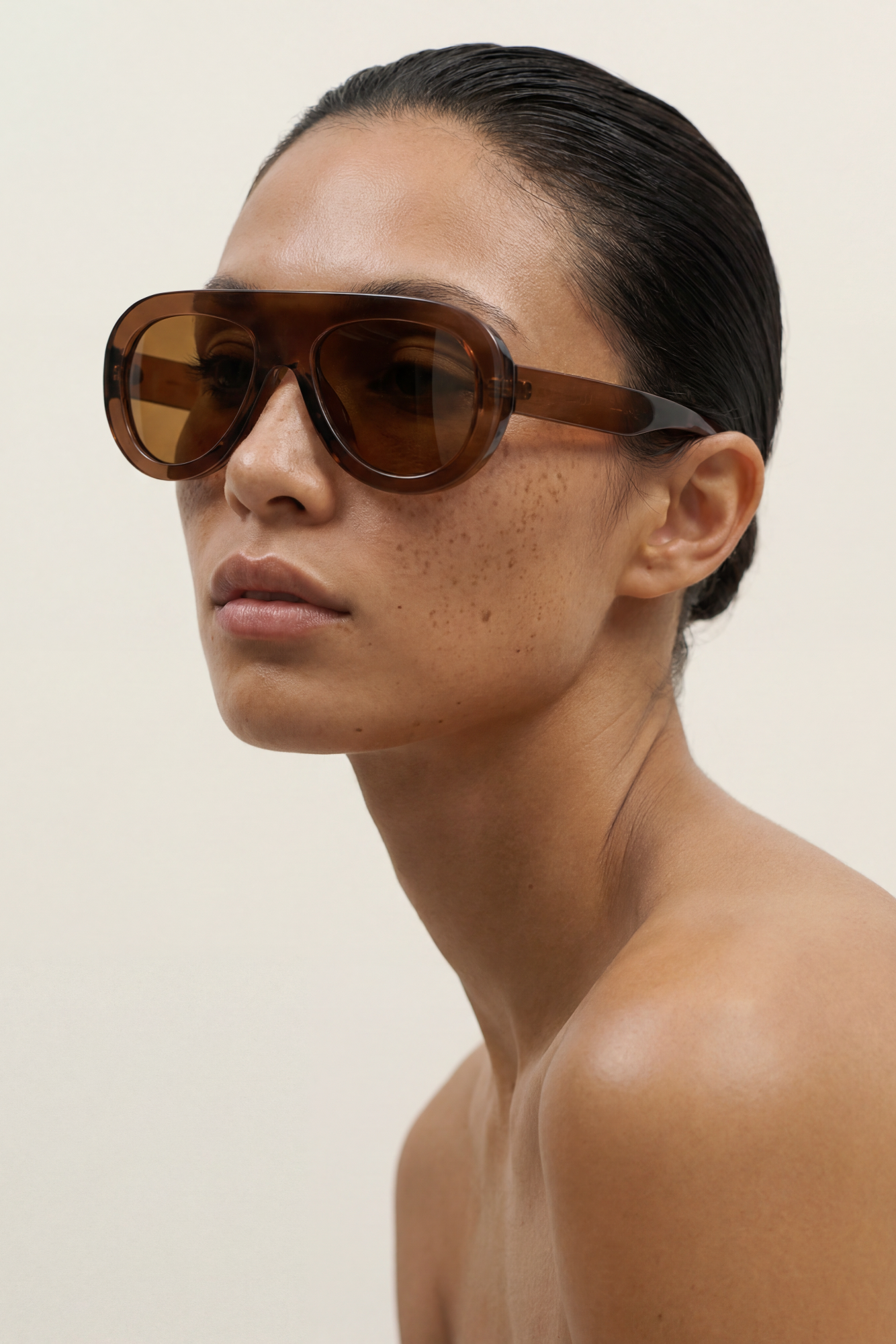 Woman wearing brown AVIATOR sunglasses against a plain background