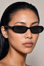 A close-up portrait of a model wearing black rectangle sunglasses against a neutral beige background.