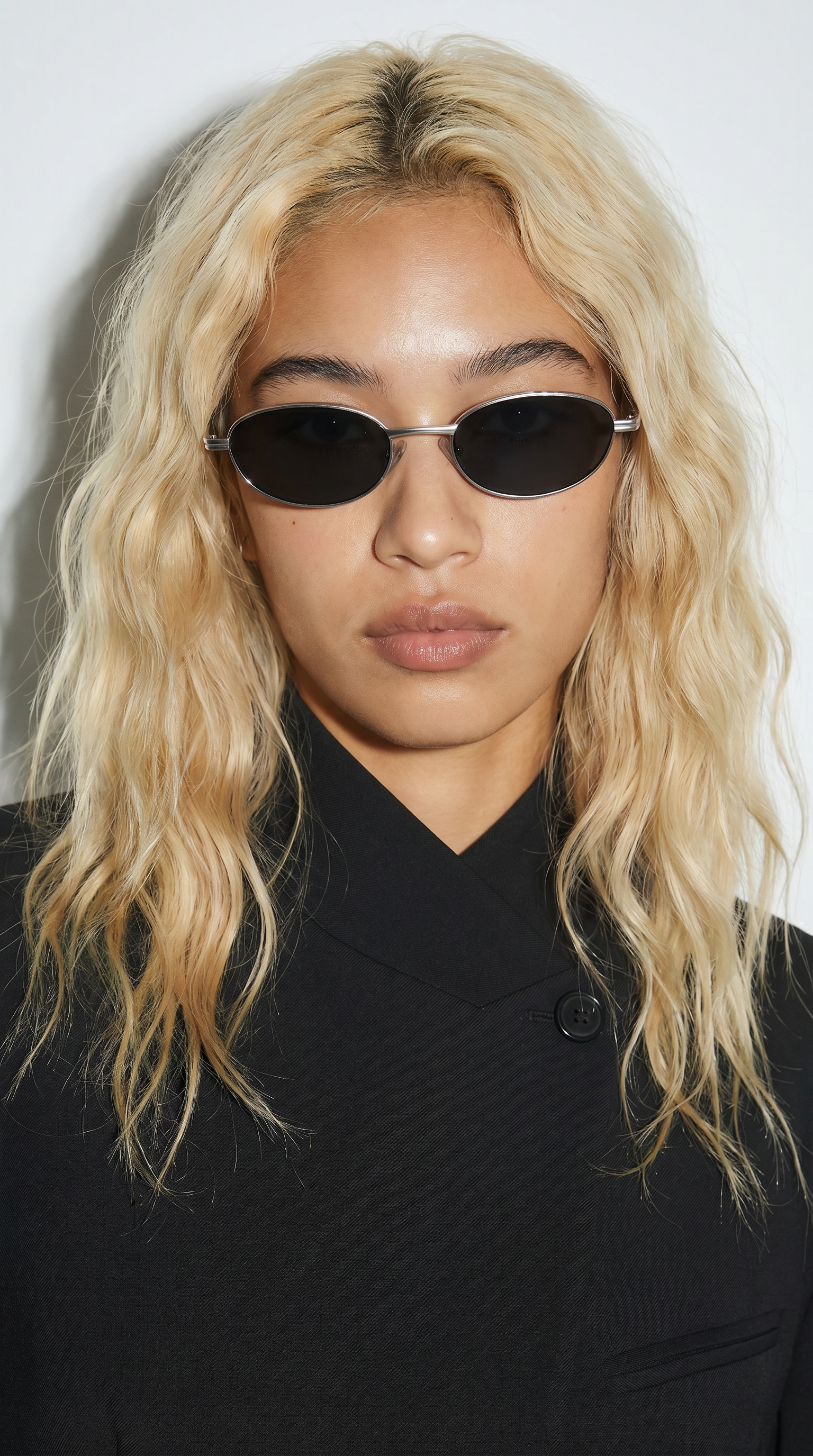 Person with blonde hair wearing black sunglasses and a black outfit against a white background