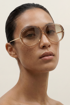 Woman wearing gold-framed sunglasses against a beige background