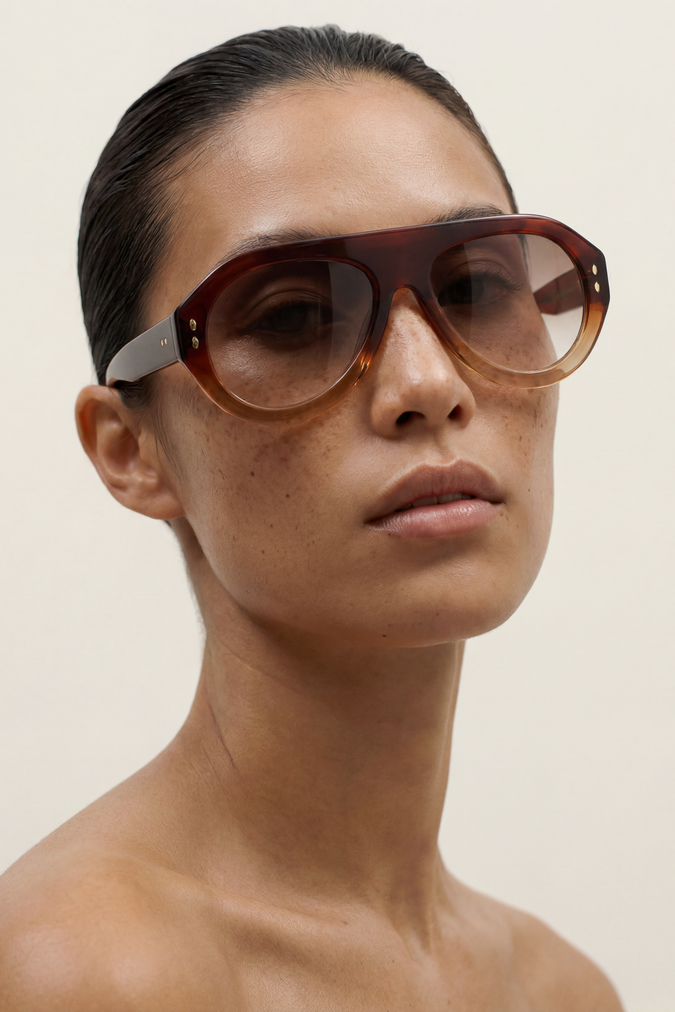 Woman wearing large brown aviator sunglasses against a plain background
