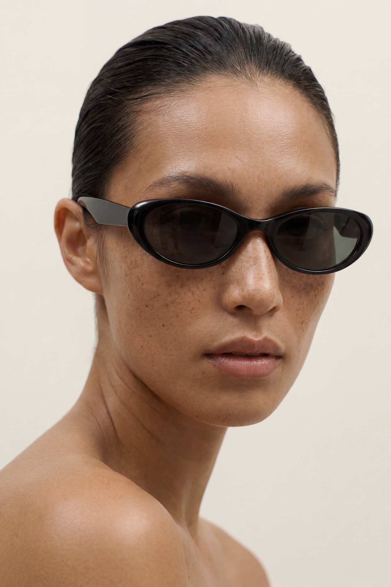 Woman wearing black cateye sunglasses against a beige background