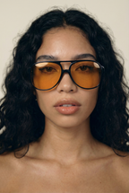 Woman wearing orange-tinted sunglasses with a neutral background