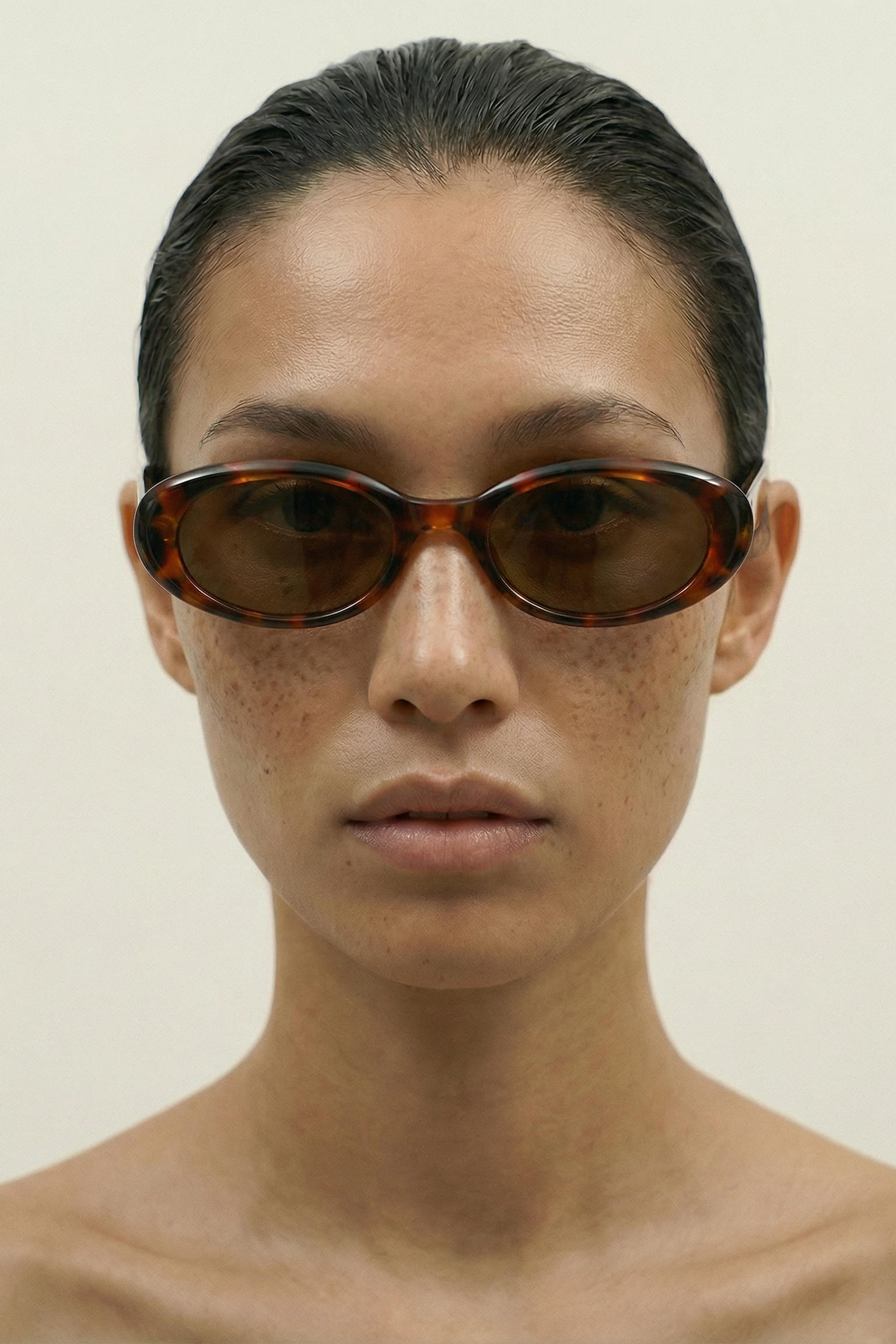 Person wearing tortoise oval sunglasses against a plain background