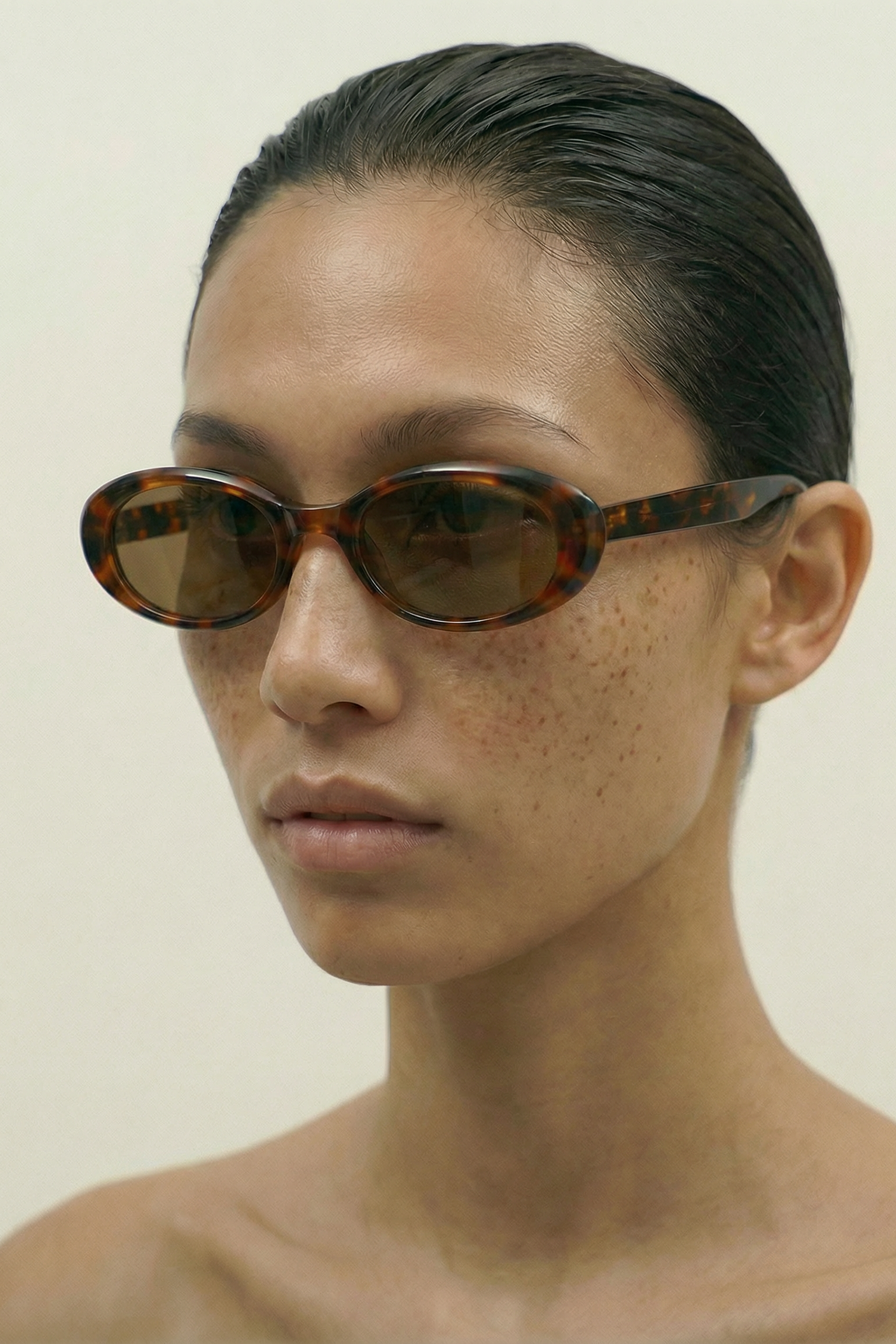 Person wearing tortoiseshell oval sunglasses against a plain background